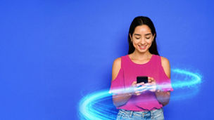 Young woman wearing fuschia top on a bright blue background texting on her phone