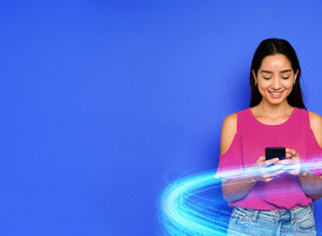 Young woman wearing fuschia top on a bright blue background texting on her phone