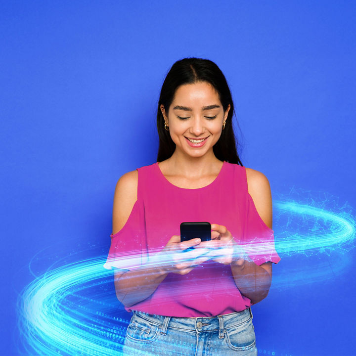 Young woman wearing fuschia top on a bright blue background texting on her phone