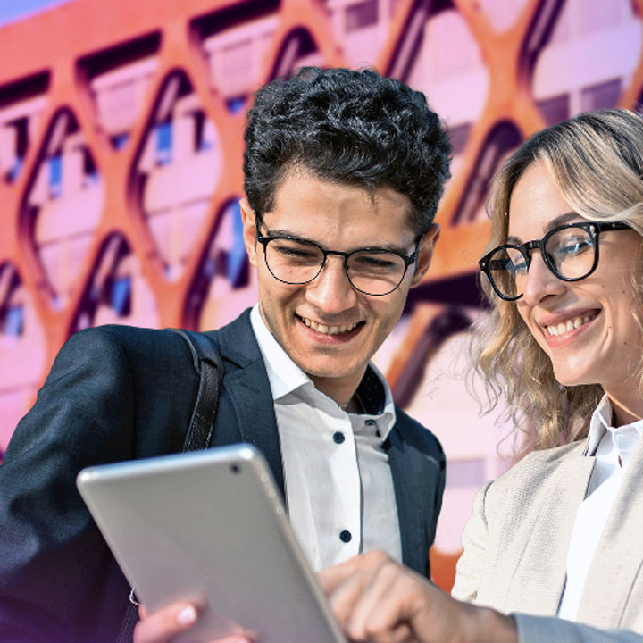 A man and a woman looking at a tablet in front of KPMG Luxembourg headquarters