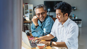 Father and adult son work on a laptop computer
