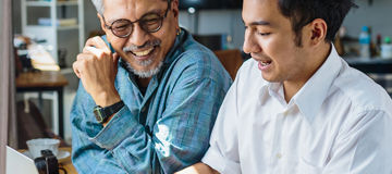Father and adult son work on a laptop computer