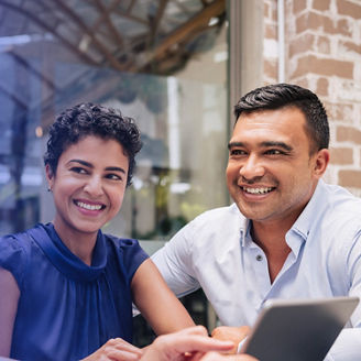 A smiling couple conducting a business meeting while looking at a tablet computer