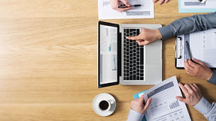 Business team hands at work with financial reports and a laptop, blank copyspace on left, top view