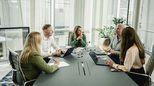 Fem ansatte sitter og diskuterer ved et motebord