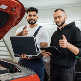 Serious focused men car technician mechanics repairing car problem of engine, during system checking detail, using tablet and laptop computer for maintenance and fixing in car garage showing thumb up.