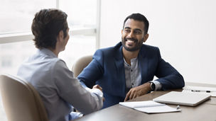 Happy young Indian business owner man shaking hands with male partner at meeting table, hiring new employee after interview, thanking financial advisor for consultation, starting partnership