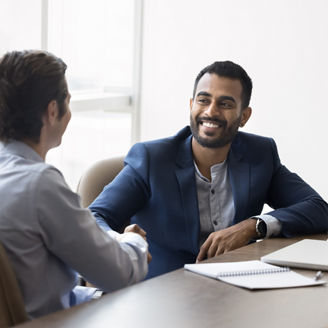 Happy young Indian business owner man shaking hands with male partner at meeting table, hiring new employee after interview, thanking financial advisor for consultation, starting partnership