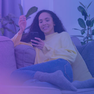 Lachende Frau mit dem Handy in der Hand auf einer Couch