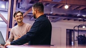 Two business men talking to each other about their tech work. Business colleagues discussing efficient ideas to finish a project. Male professionals working in a startup.; Shutterstock ID 2300432543; purchase_order: advisory assurance marketing; job: anne; client: ai-hub