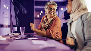 Two happy businesswomen having a discussion while working at their desks in an office. Diverse businesswomen working as a team in a creative co-working office.; Shutterstock ID 2274258875; purchase_order: advisory assurance marketing team; job: anne rouschop; client: hyperautomation