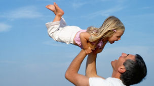 Father holding up daughter (2-4) on beach, smiling, close-up