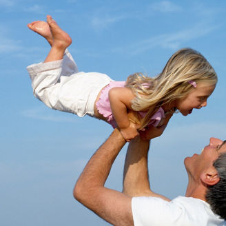 Father holding up daughter (2-4) on beach, smiling, close-up