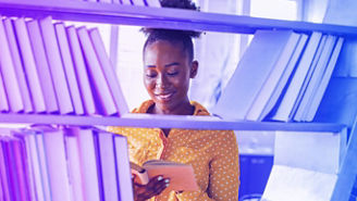 Education, high school and knowledge concept - African student woman with books over shelves in librarry. African american girl reading book in library