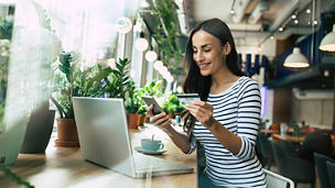 Beautiful smiling young woman using laptop and doing shopping online with help of her smartphone and card