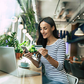 Beautiful smiling young woman using laptop and doing shopping online with help of her smartphone and card