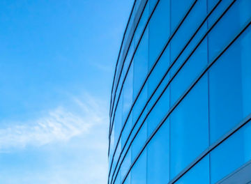 Building exterior with bright blue sky background. Building exterior with bright blue sky in the background on a sunny day. The interior of the building can be seen through the large glass windows.