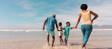 African american grandparents holding hands of grandchildren and running in sea against sky. summer, nature, copy space, unaltered, family, love, togetherness, childhood, enjoyment, holiday.