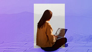 Woman sat down using her laptop with mountains in the distance