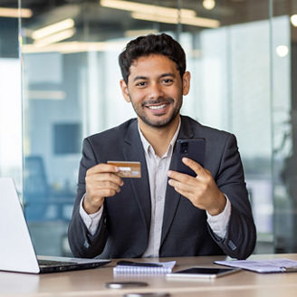 Portrait of young successful Asian businessman inside office, man looking at camera smiling, using online application on phone for internet shopping, holding bank credit card in hand.