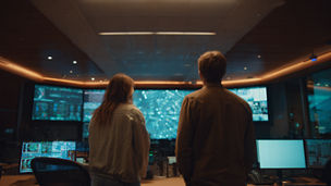 Wide shot from behind two colleagues stand in front of a large screen in a modern control room, strip lighting gives it a modern edge, windows to the side of the room give subtle warm lighting, shallow depth of field, cinematic lighting, professional lens bokeh, ultra-detailed photorealism, beautifully composed, 8k resolution, --ar 16:9 --v 7 Job ID: f0e34bf8-c7ca-42d2-8406-4ffc8187ebfd