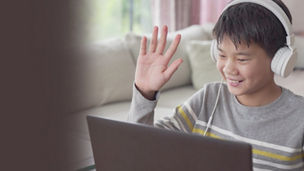 Boy sitting in front of laptop wearing headphones and waving hand banner