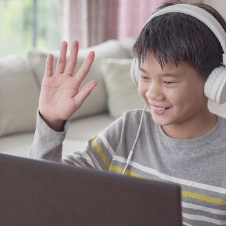 Boy sitting in front of laptop wearing headphones and waving hand banner