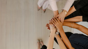 Top view image of group of young women colleagues putting their hands together with copy space. Business coworkers with stack of hands showing unity.