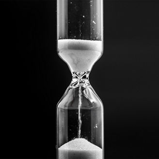 Glass hourglass with white sand , closeup on black background, time concept