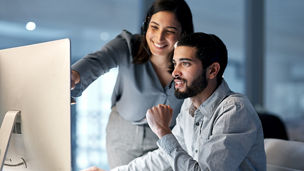 Shot of a young woman helping her colleague in a call centre late at night