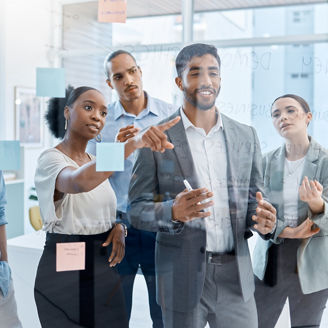 Teamwork, collaboration and planning with a team and their manager working on the vision, mission and strategy for their business. Writing on a glass wall with sticky notes for growth and development.