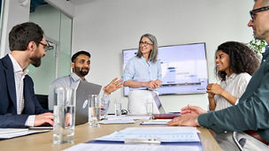 Diverse executive team people discussing company strategy at board meeting. Multicultural employees with senior leader listening indian manager brainstorming working sitting at table in office.