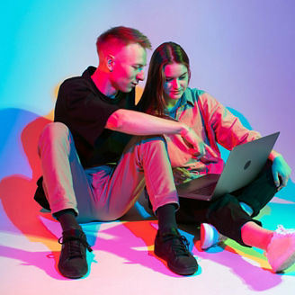 Stylish young couple with laptop working, watching series or shopping online. Colorful neon light. High quality photo