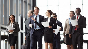 Young elegant woman with paper pointing right while showing colleagues new conference hall for running political events