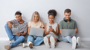 Teenagers with different devices sitting near light wall