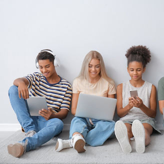Teenagers with different devices sitting near light wall