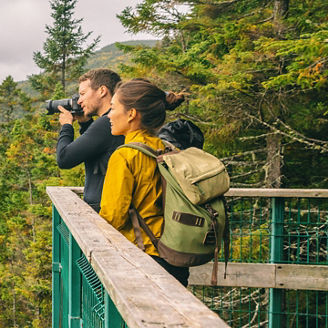 Travel couple hikers tourists taking photo with camera at view of mountain landscape in Autumn forest Parc de la Jacques Cartier, Quebec, Canada. Panorama banner background.