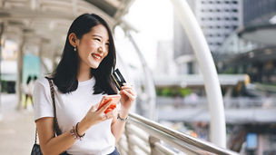 Business people shopping via online application media concept. Happy smile young adult asian woman consumer using creadit card and smartphone. City on day background with copy space.