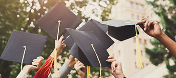 A group of multietnic students celebrating their graduation by throwing caps in the air closeup. Education, qualification and gown concept.