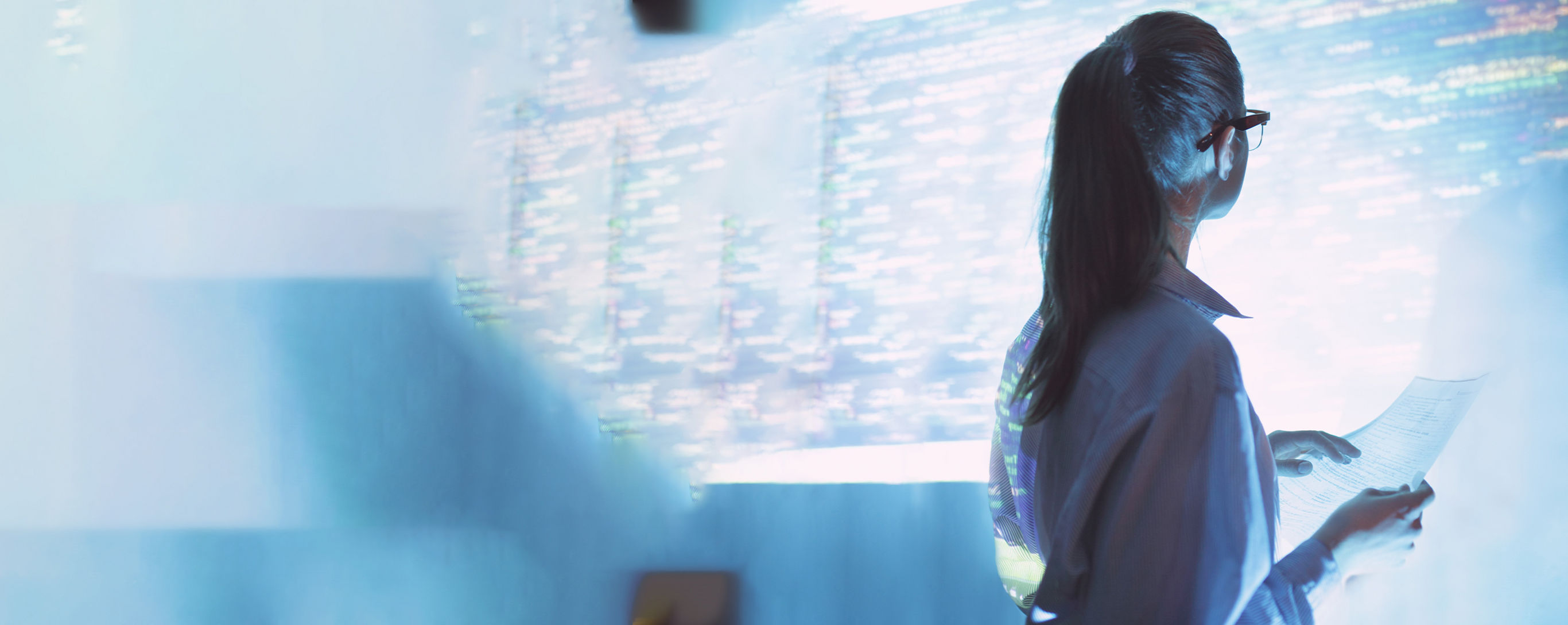 Mujer de espaldas con lentes viendo una pantalla