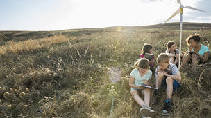 Group of children working sitting with dummy windmill in grass field