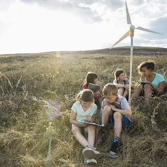 Group of children working sitting with dummy windmill in grass field