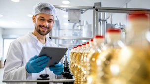 Technologist holding tablet computer and checking production of bottled refined sunflower oil in food factory production line.
