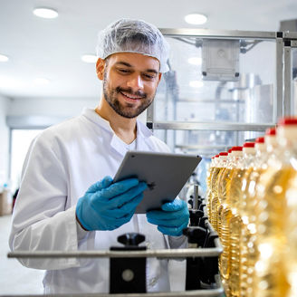 Technologist holding tablet computer and checking production of bottled refined sunflower oil in food factory production line.