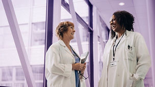 Low angle view of happy female physician with hands in pockets discussing with colleague at hospital