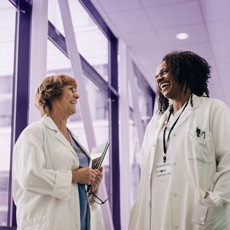 Low angle view of happy female physician with hands in pockets discussing with colleague at hospital