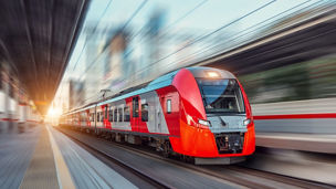 Electric passenger train drives at high speed among urban landscape.