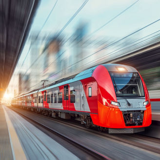 Electric passenger train drives at high speed among urban landscape.