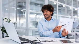 Portrait successful businessman, Latin American man shows a report of financial documents online interlocutors in the laptop screen, an employee inside an office building online video conference.