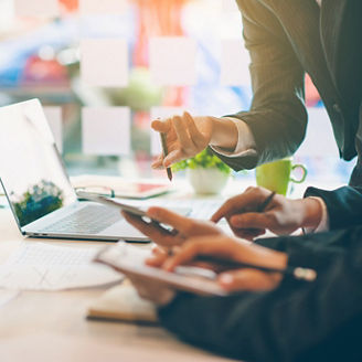 Three people working at a desk with a laptop, smartphone, and documents during a business discussion